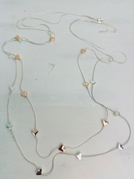 close-up of a long double-chain mixed metal heart charm necklace with a silver and gold hearts 