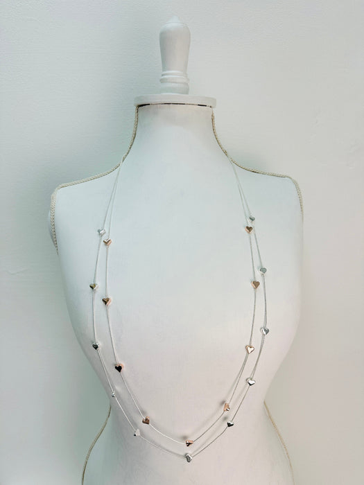 A long double-chain mixed metal heart charm necklace with a silver and gold hearts displayed on a mannequin