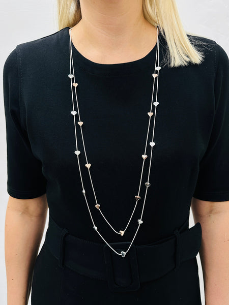 A long double-chain mixed metal heart charm necklace with a silver and gold hearts displayed on a model