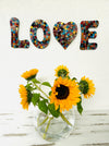 display view of mosaic love on the wall with a vase of sunflowers below