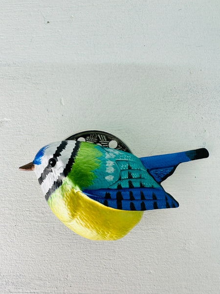 A magnetic brooch depicting a blue tit bird with blue, green, and yellow feathers.