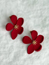matte red flower-shaped stud earrings with gold centers on a white textured background