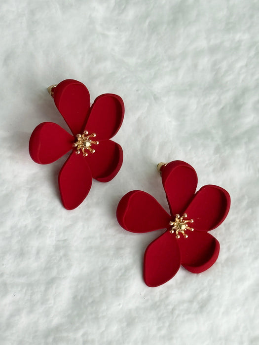 matte red flower-shaped stud earrings with gold centers on a white textured background
