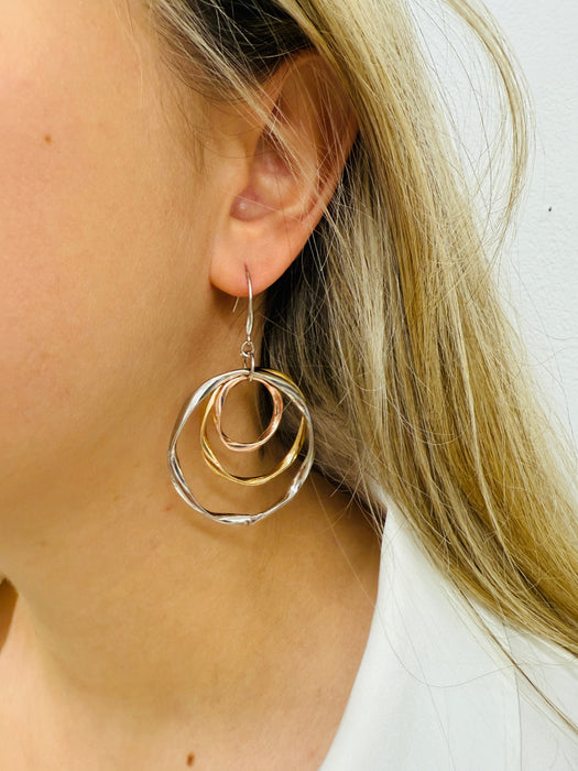 A close-up image of a woman's ear wearing a silver and gold tone interlocking rings dangle earring.
