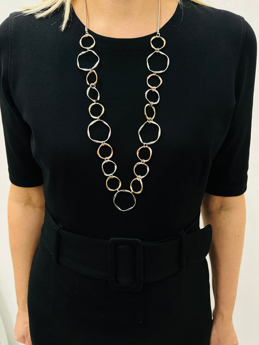 A person wearing a black dress with a Victoria necklace consisting of open circles in silver, gold, and rose gold tones.
