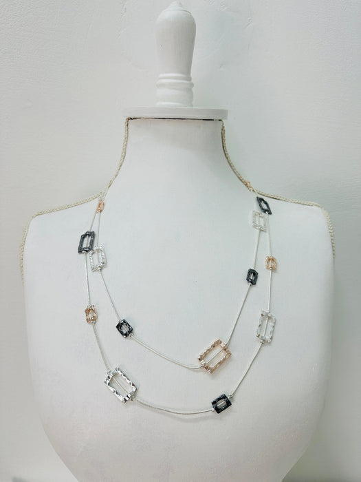 A multilayered necklace with silver-colored chains and clear, black, and pink square beads displayed on a mannequin bust