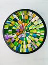 Top view of handmade mosaic bowl in bright citrus glass pieces forming circular pattern on white surface.