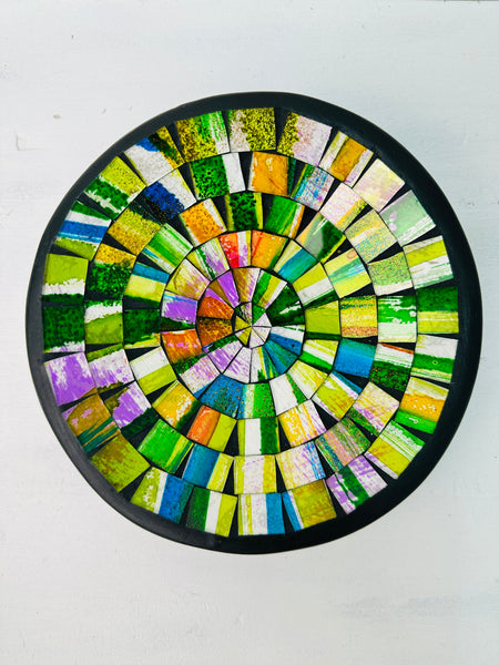 Top view of handmade mosaic bowl in bright citrus glass pieces forming circular pattern on white surface.