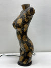 A sculptural female torso lamp or decorative figure with a glossy black and gold crackle mosaic pattern, standing on a black circular base against a light gray wall.