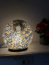 Handmade black and gold mosaic donut lamp illuminated with warm white LED light, creating a soft ambient glow on a table surface