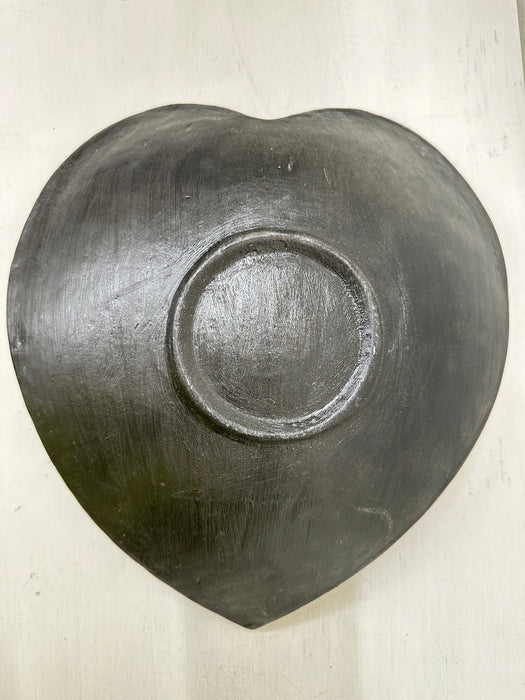Underside of handmade mosaic heart bowl showing smooth terracotta base and curved heart shape on white background.