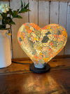 Heart-shaped mosaic lamp glowing warmly with rainbow glass pieces.