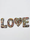 A mosaic wall piece with the word 'LOVE' broken down into individual letters, each painted in a spectrum of colors.