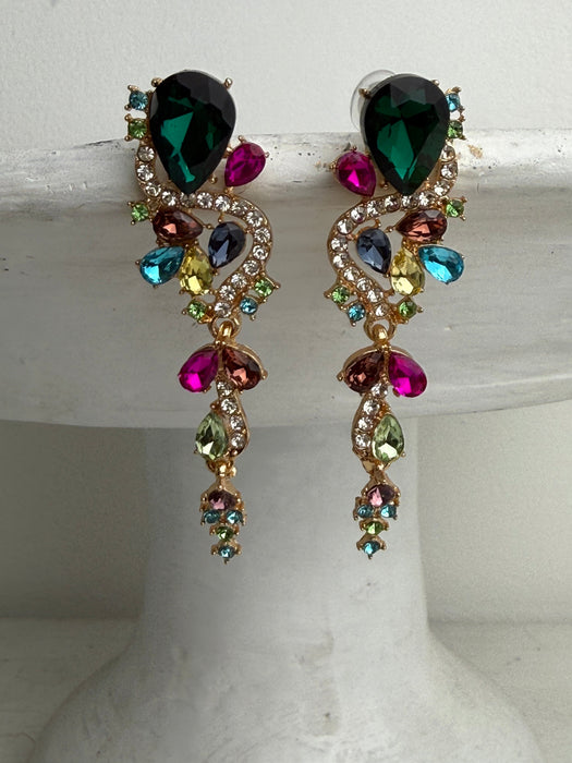 A pair of gold-tone statement dangle earrings with large faceted dark green teardrop stones and multiple colorful rhinestones in pink, blue, yellow, and green, displayed on a white jewelry stand.