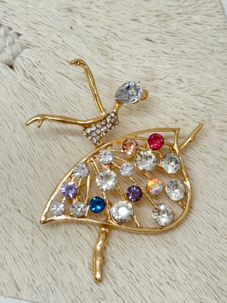 A gold-tone brooch in the shape of a ballerina with multicolored gemstones on it.