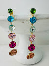 A pair of multicolored gemstone earrings with gold-colored mountings displayed on a white stand.