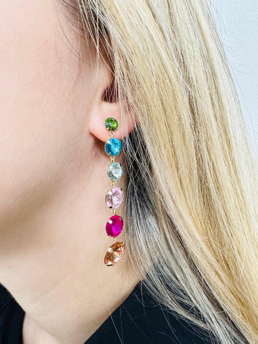 A person wearing a pair of multicolored stone earrings with a drop design.