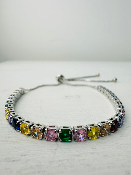 An adjustable bracelet with a silver metal bar and multicolored rainbow crystal details.