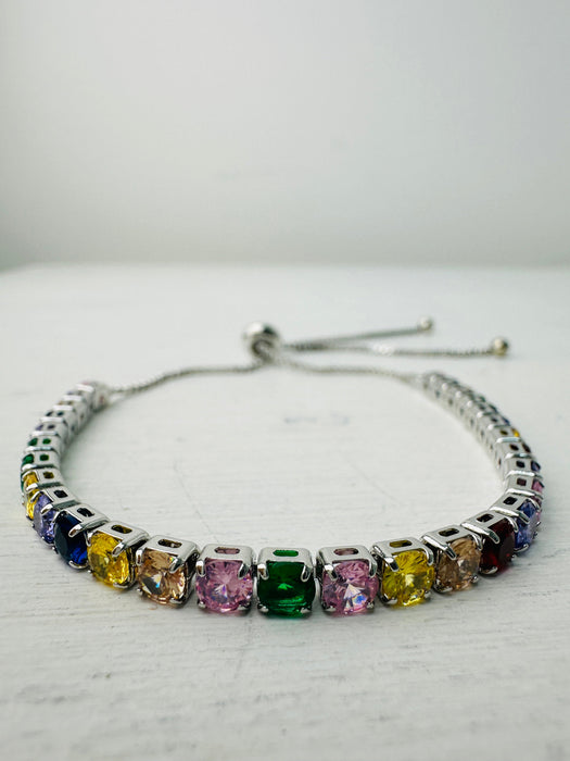 An adjustable bracelet with a silver metal bar and multicolored rainbow crystal details.