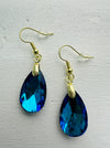 A pair of teardrop-shaped earrings with ocean blue crystals set in gold-colored settings, displayed against a white background.