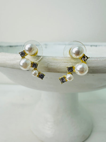 A pair of pearl stud earrings with gold accents and small crystal embellishments displayed on a white stand.