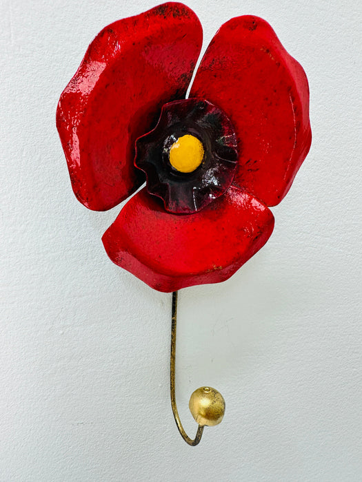 Handmade and hand painted red poppy hook with yellow and antique gold detailing, mounted on a wall.