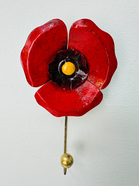 Handmade red poppy flower metal wall hook with gold detailing on white background.