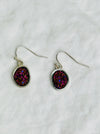 Pair of earrings with purple and pink druzy stones on a white background
