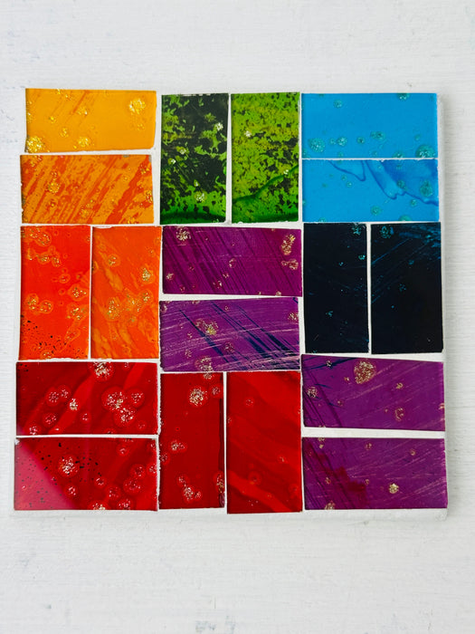 Square rainbow mosaic coaster featuring colourful hand-painted glass pieces arranged in a geometric layout on MDF base, photographed from above on a light surface.