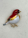 Bird-shaped brooch with red and gold colors on a light gray background
