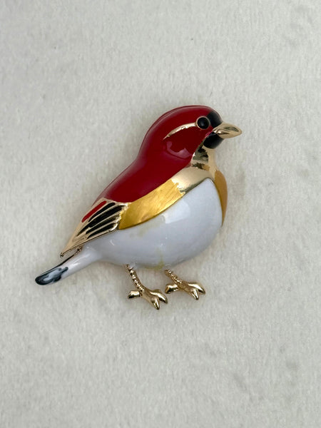 Bird-shaped brooch with red and gold colors on a light gray background