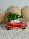 Festive enamel brooch featuring a classic red car carrying a green Christmas tree topped with a golden star