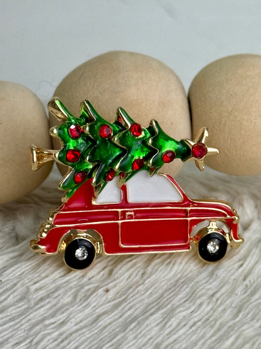 Festive enamel brooch featuring a classic red car carrying a green Christmas tree topped with a golden star