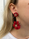 A person wearing red floral drop earrings with gold hoops.