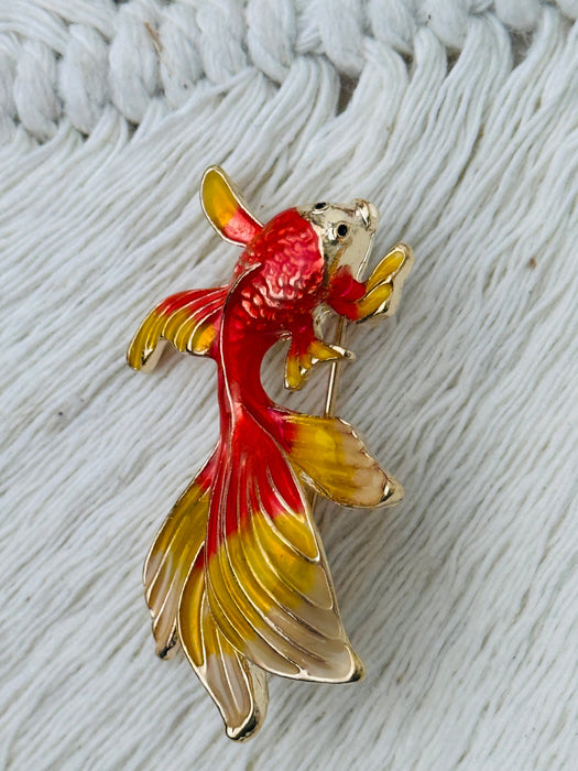 Goldfish-shaped brooch with red and yellow colours on a textured white background
