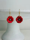 Red flower-shaped earrings on a white stand with a white background