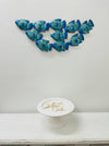 Small reef fish shoal metal wall art hanging above a white table in a home interior.
