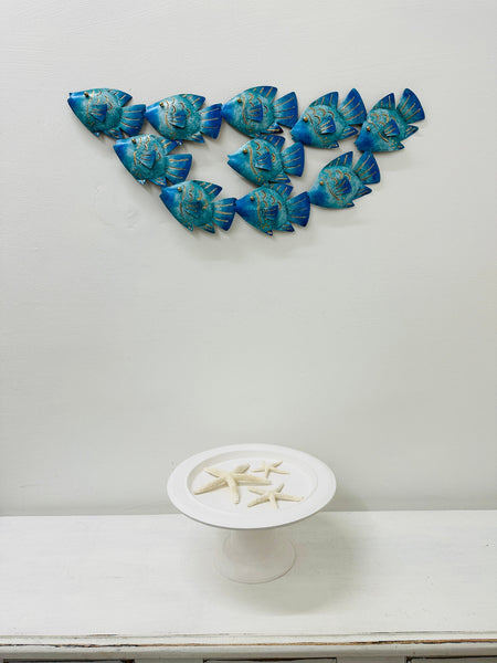 Small reef fish shoal metal wall art hanging above a white table in a home interior.