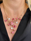 Rose gold floral necklace with enamel flowers in soft pink deep rose and pearl tones, and small pink crystal accents on brach style design, displayed on a model.