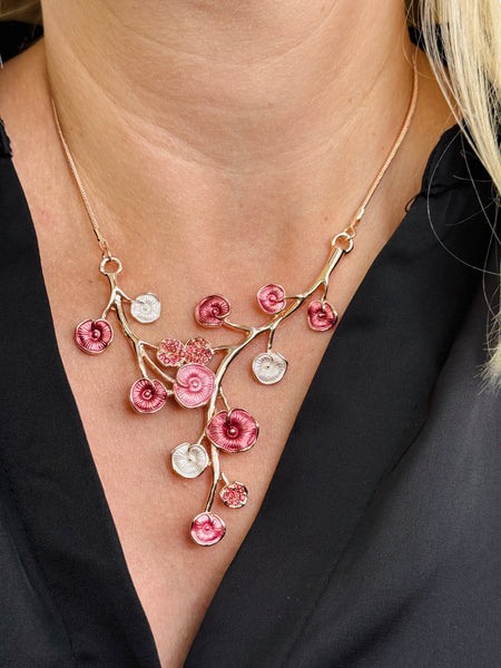 Rose gold floral necklace with enamel flowers in soft pink deep rose and pearl tones, and small pink crystal accents on brach style design, displayed on a model.