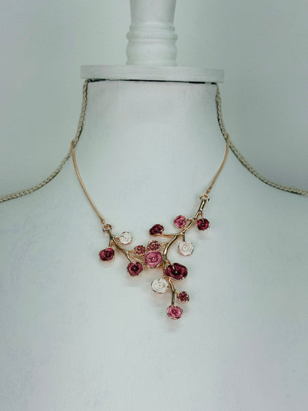 Rose gold floral necklace with enamel flowers in soft pink, deep rose and pearl tones, and small pink crystal accents on brach style design, displayed on a mannequin.
