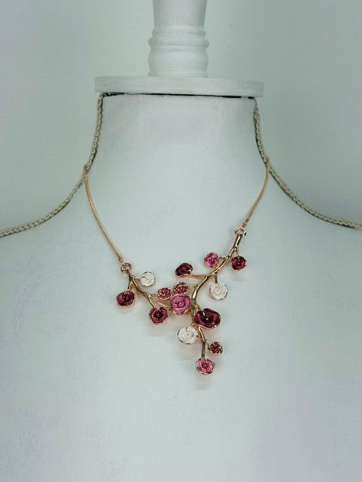 Rose gold floral necklace with enamel flowers in soft pink, deep rose and pearl tones, and small pink crystal accents on brach style design, displayed on a mannequin.