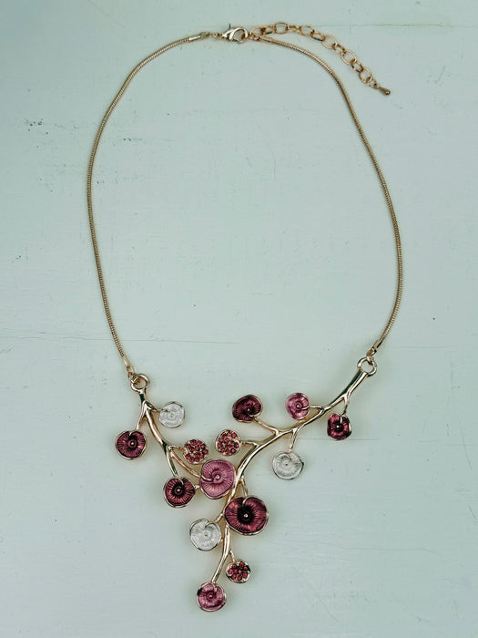 Rose gold floral necklace with enamel flowers in soft pink, deep rose and pearl tones, and small pink crystal accents on brach style design, displayed on a table.