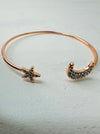 A rose gold cuff bracelet with a simple moon and star design, featuring black stones on the star and moon accents.