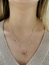 Rose gold heart-shaped necklace worn by a person with a neutral background