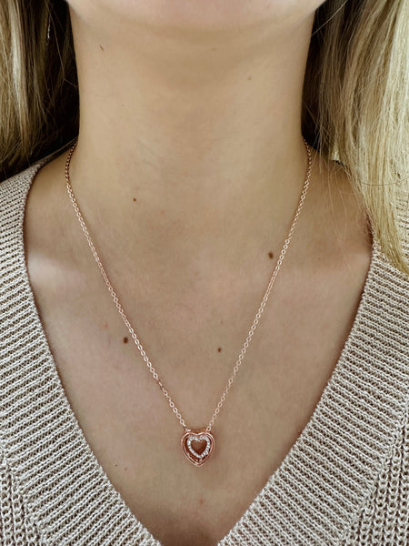 Rose gold heart-shaped necklace worn by a person with a neutral background