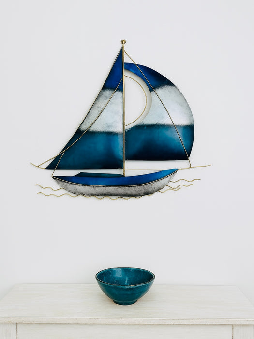 Hand-painted blue and silver metal sailing boat wall sculpture displayed above a small bowl