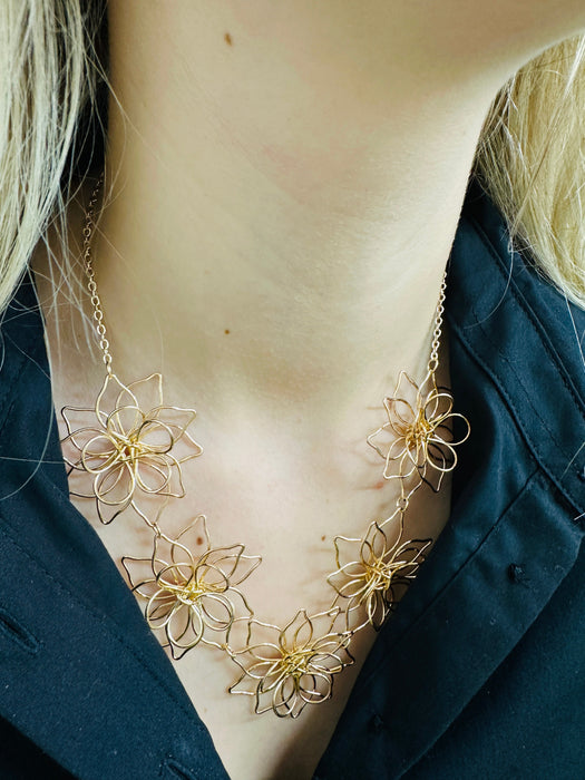 A gold-coloured necklace with flower details, displayed on a model