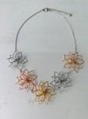 Necklace with floral pendants in silver, rose gold, and gold on a light gray background