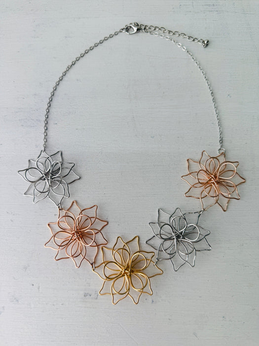 Necklace with floral pendants in silver, rose gold, and gold on a light gray background